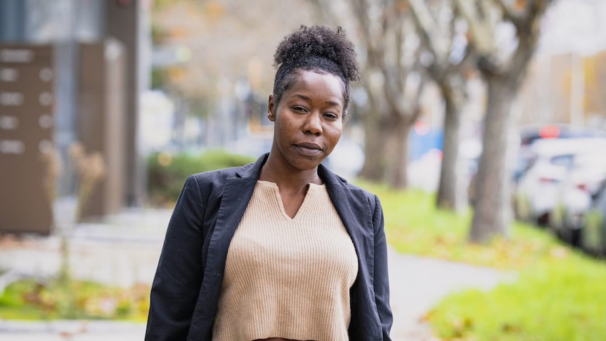 A woman in a blazer standing on the street and looking at the camera.