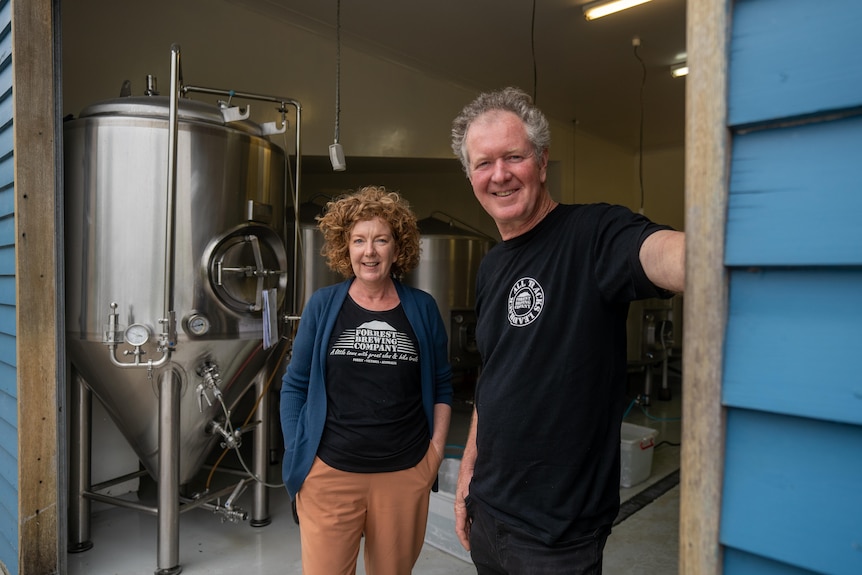 Sharon and Matt stand in a shed with big vats behind them. 