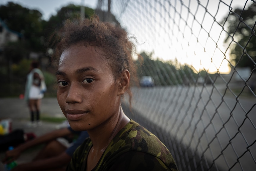 Woman sitting next to a metal fence.