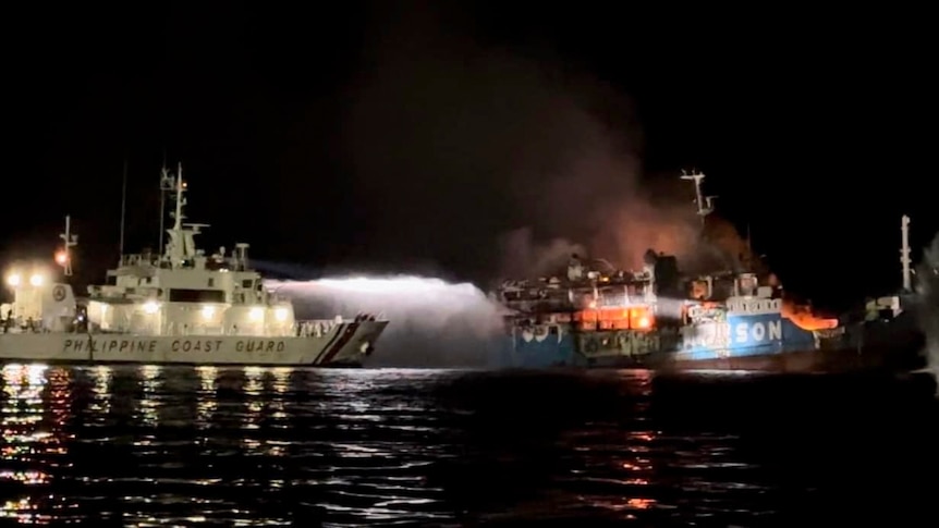 A ship near another vessel on fire taken at night. 