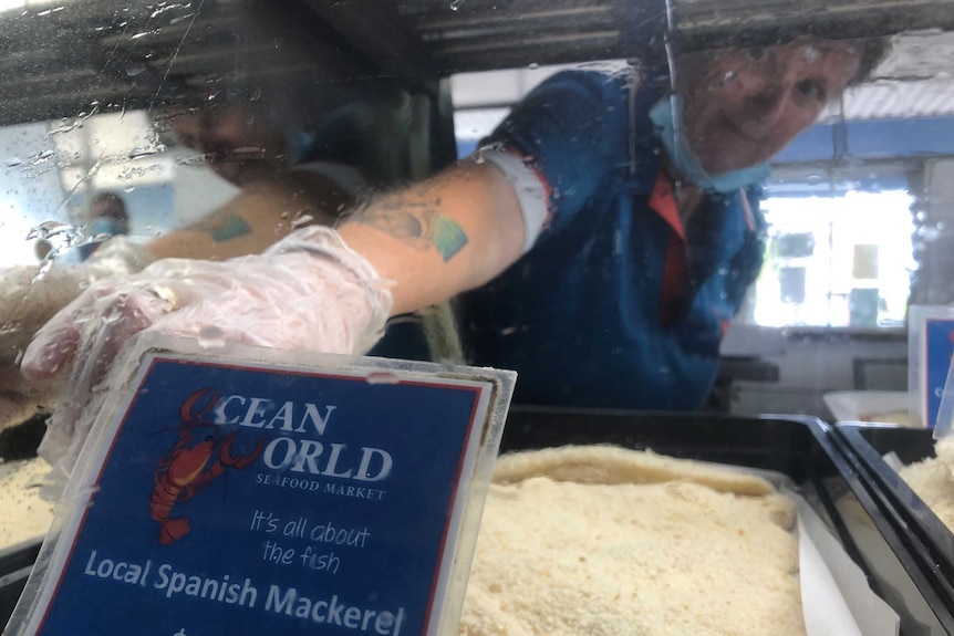 A retail assistant reaches into the chilled cabinet of locally caught, crumbed Spanish mackerel fillets ready for the deep fryer