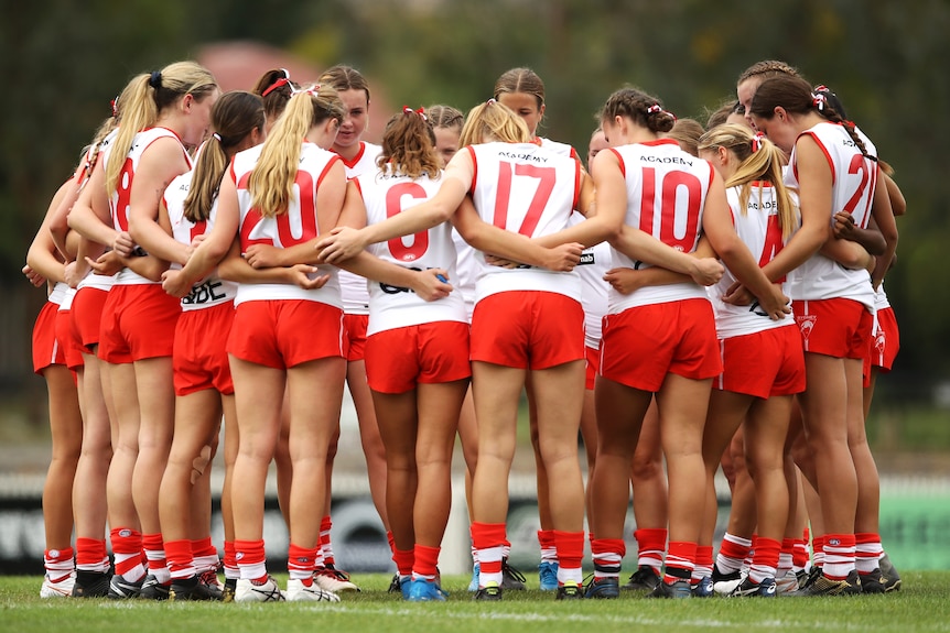 A Sydney Swans team stands in a huddle with arms around each other