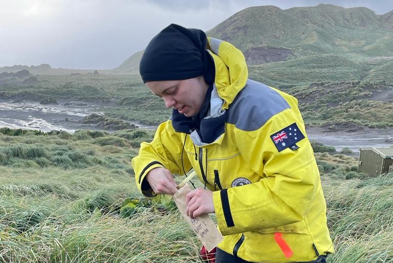 Kita Williams, dressed in a bright yellow jacket, collecting plant samples in remote wilderness location.