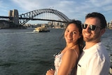Man and woman smile, pictured in front of Sydney Harbour Bridge
