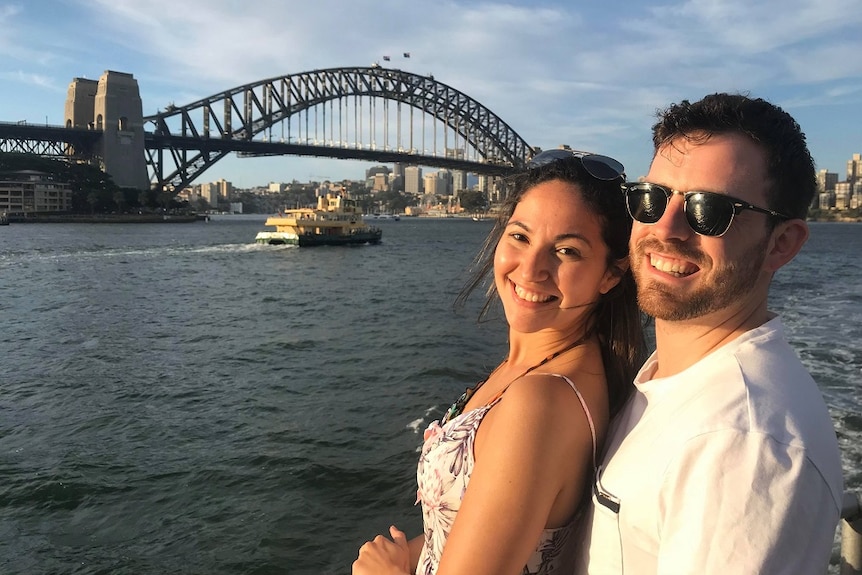 Man and woman smile, pictured in front of Sydney Harbour Bridge
