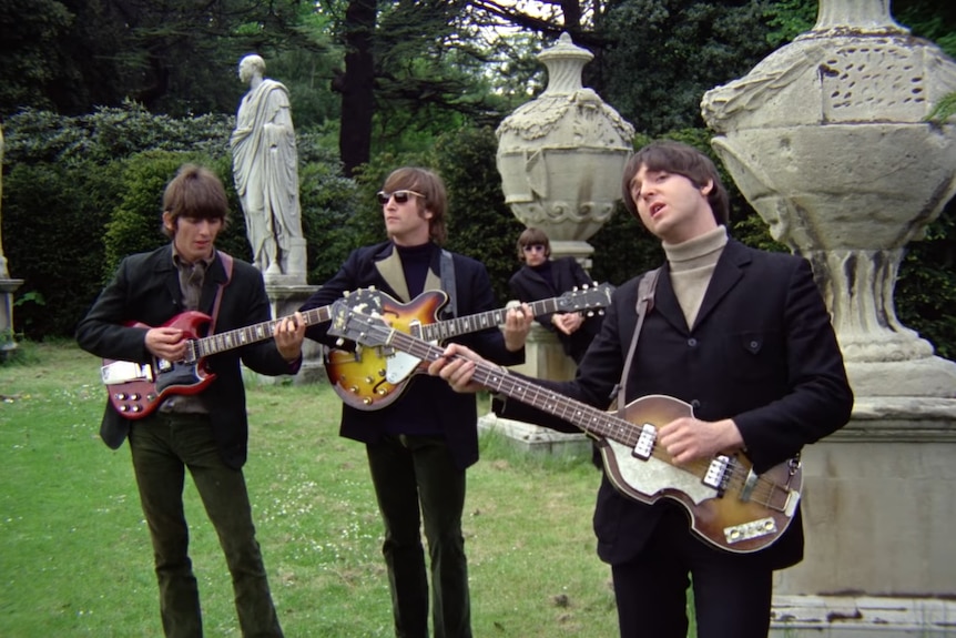 The Beatles stand in a garden miming to a backing track on their guitars.