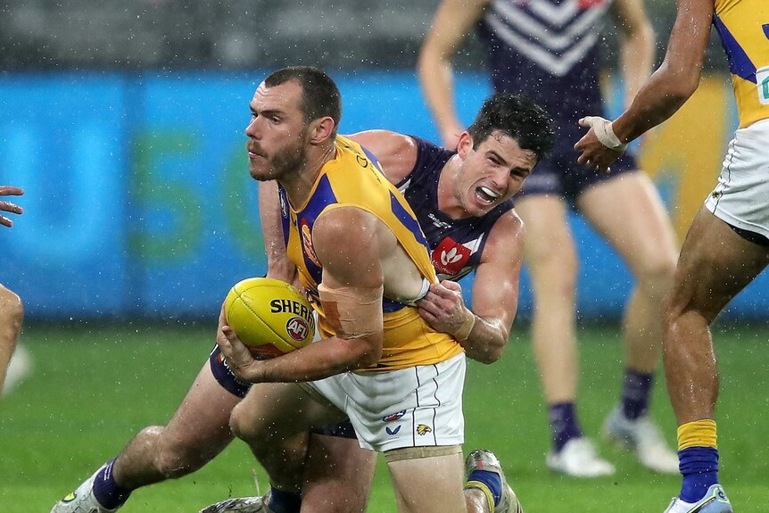 A football player in purple tackles another player in yellow.