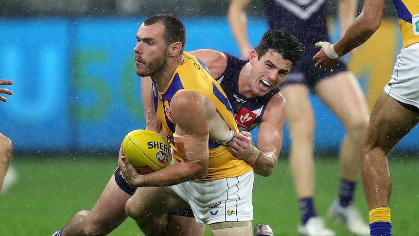 A football player in purple tackles another player in yellow.