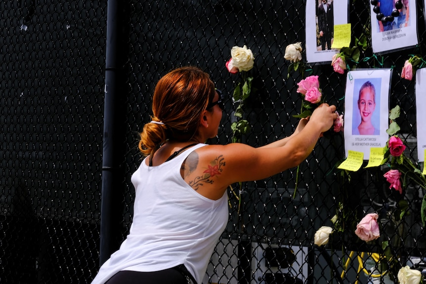 A young tattooed woman places a flower on a memorial fence showing girl's photograph.