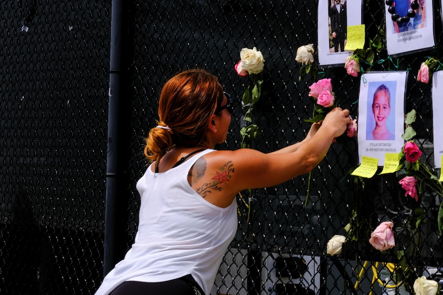 Una giovane donna tatuata mette un fiore su una ringhiera commemorativa che mostra il ritratto della ragazza.