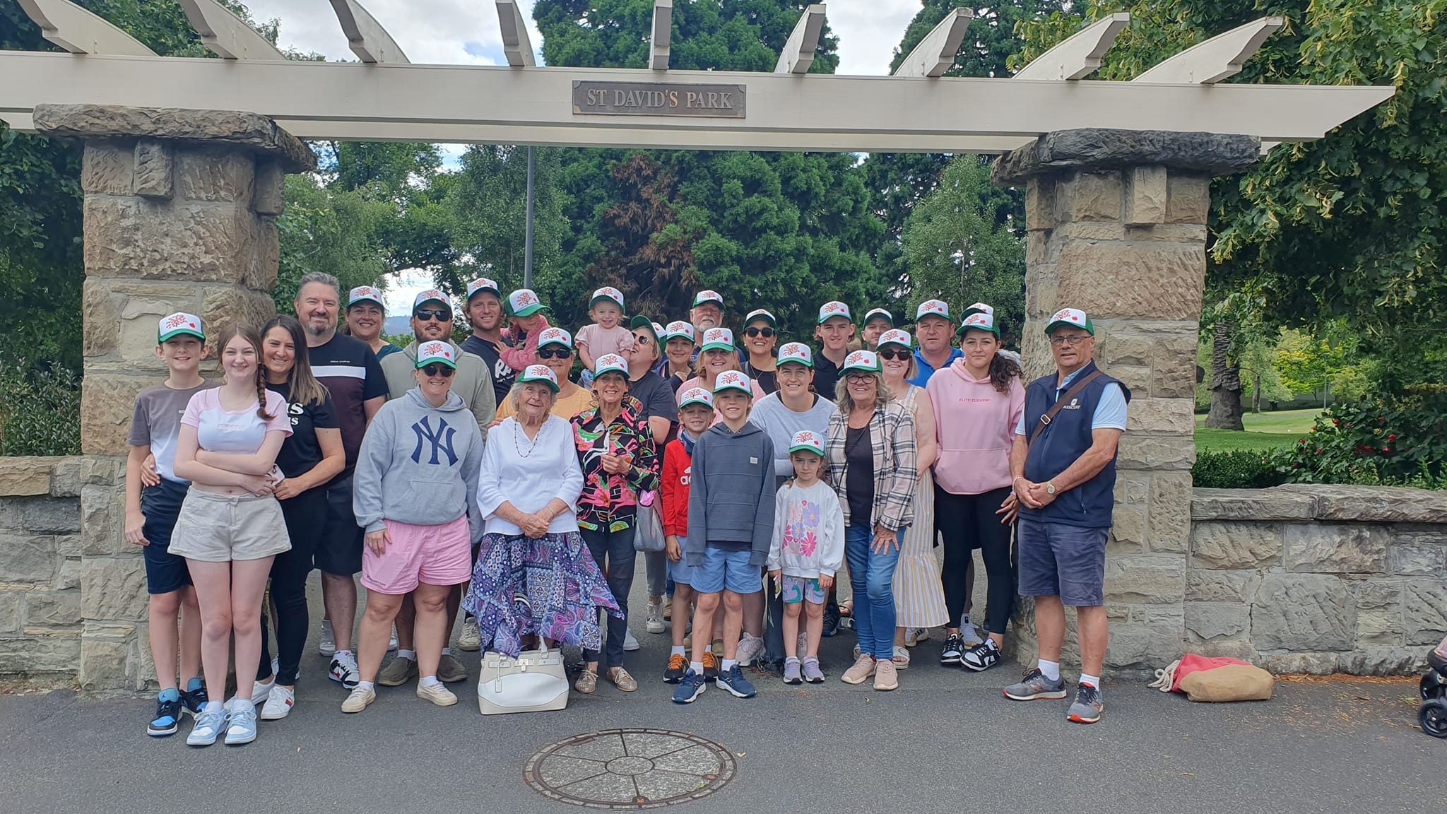 A family standing under a sandstone and wooden entry to a park. Theres approx 30 people in the frame.