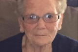 An elderly woman wearing glasses and looking at the camera.