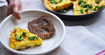A slice of frittata in a bowl with bread alongside a pan of frittata, perfect for a weekend brunch.