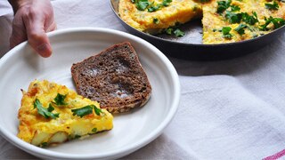 A slice of frittata in a bowl with bread alongside a pan of frittata, perfect for a weekend brunch.