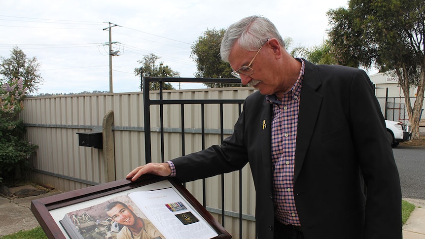 Doug Baird looks at book with images of his late son, Cameron Baird VC.