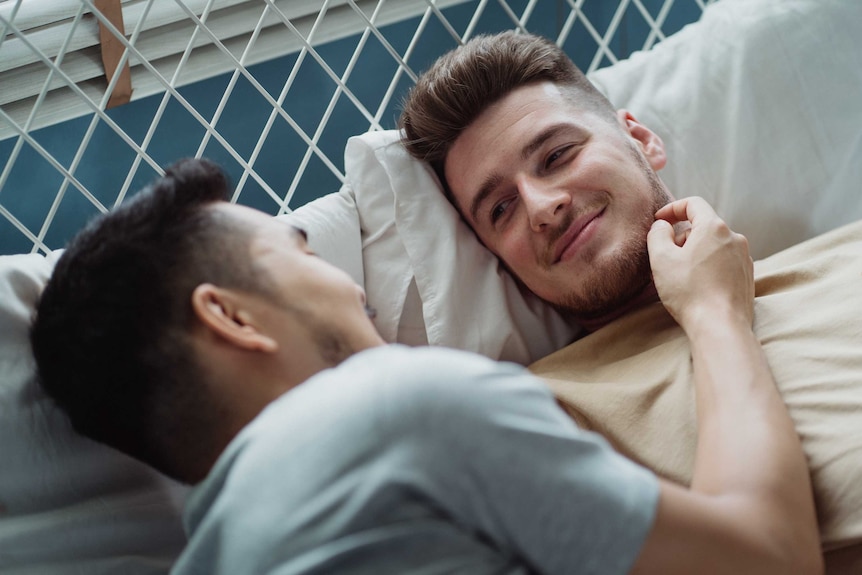 Two men lay in bed looking at one another