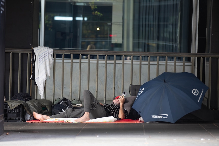 A man lying down with an open umbrella next to him surrounded by bags