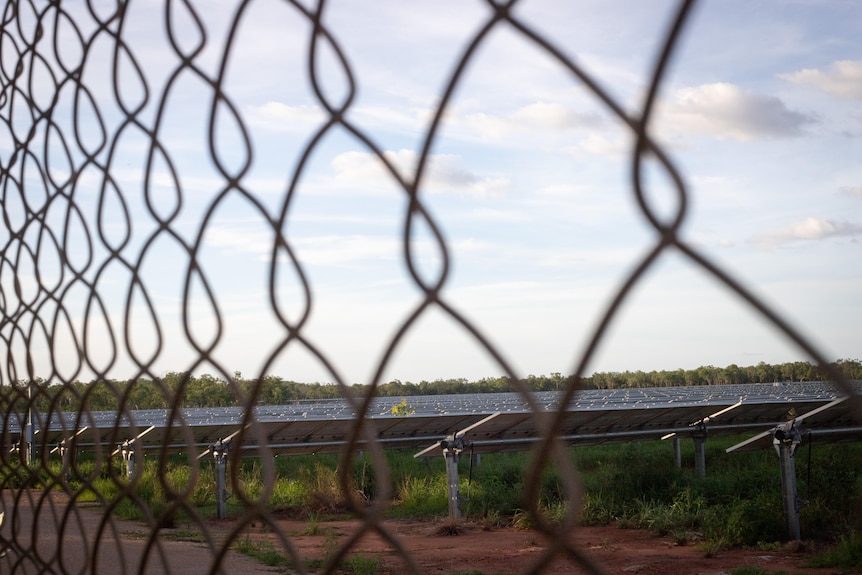 Rows of solar panels behind a wire fence.