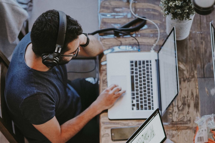 A man wearing headphones looks at a laptop computer.