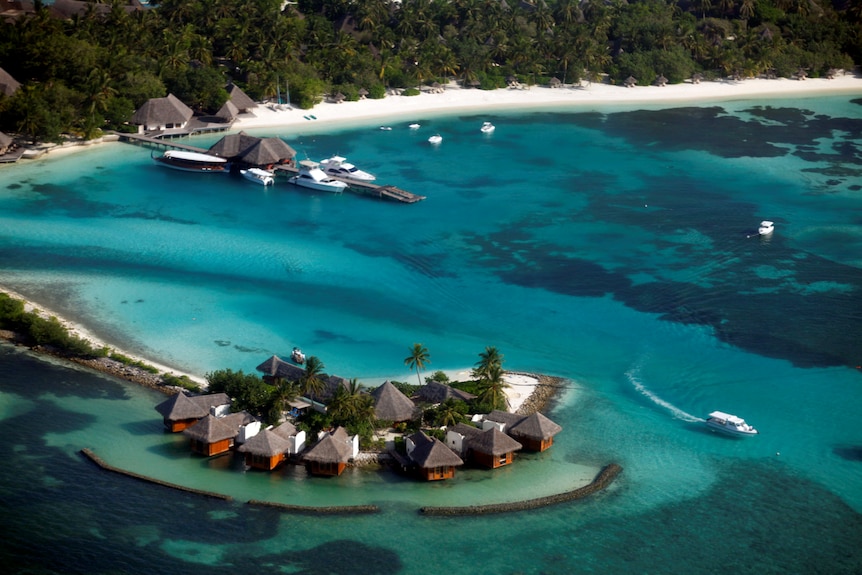 An aerial shot of a tropical blue lagoon, with beachfront bungalows, resorts and yachts.