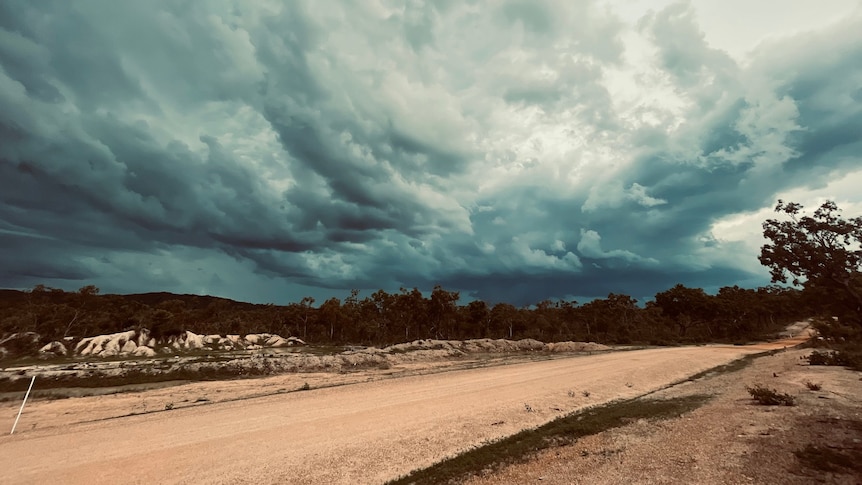 storm clouds form over a dirt road in scrubby bushland