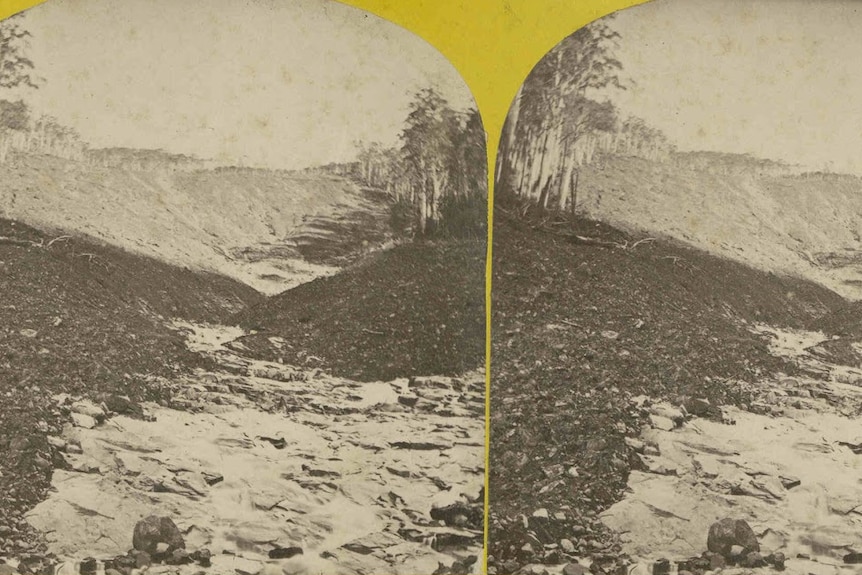 A black and white mounted stenograph of water flowing through a gully, land has been washed away