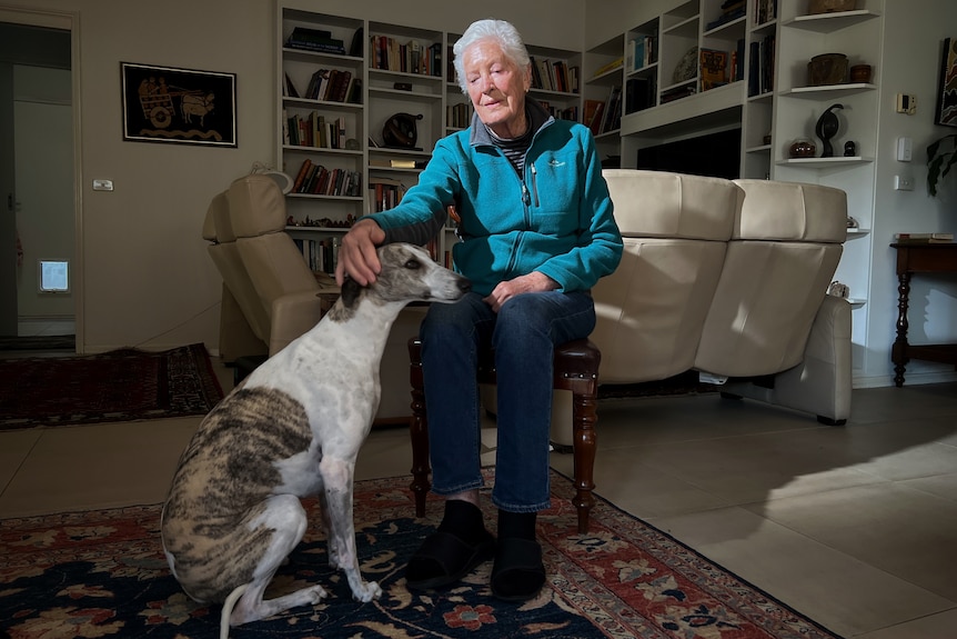 Kath sits in an armchair and pats her dog's head.