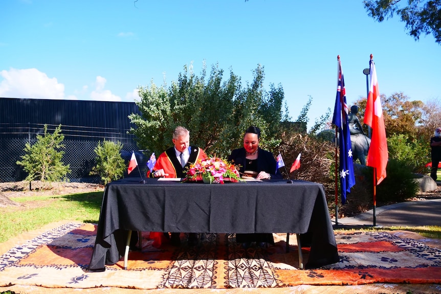 A man and women sit at a table signing a document.