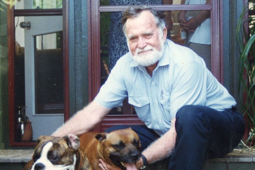 Man sits on steps with two dogs and smiles while patting them.