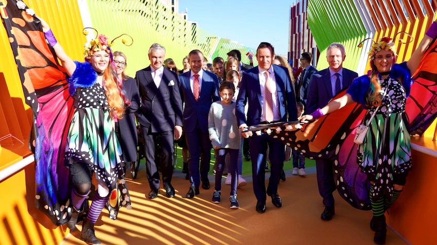 Performers in costume, children and MPs walk across a colourful bridge.