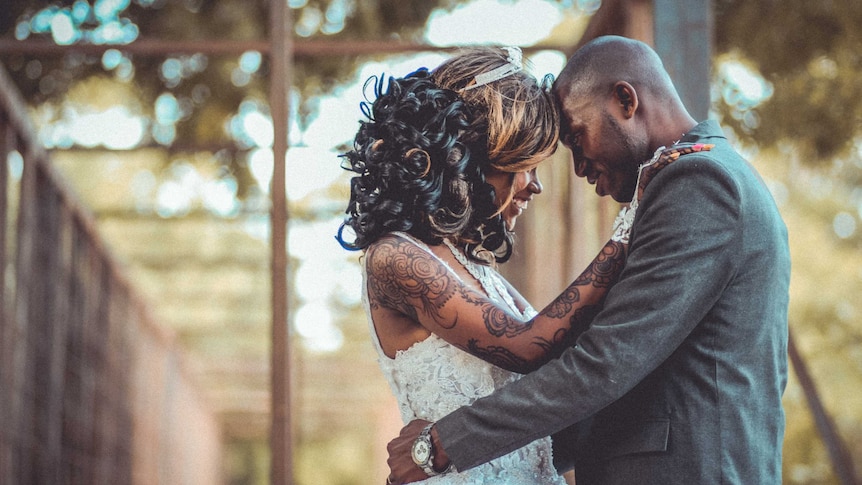 A bride and groom hugging and the bride has tattoos along her whole arm for a story about the reasons behind hiding tattoos.