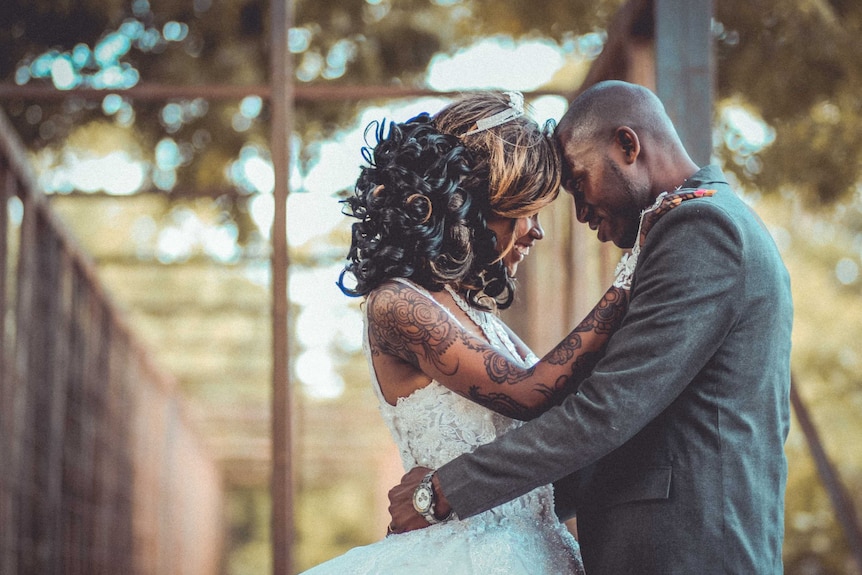 A bride and groom hugging and the bride has tattoos along her whole arm for a story about the reasons behind hiding tattoos.