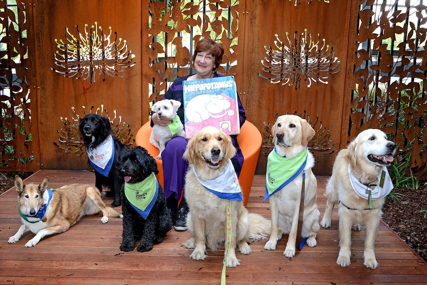 Author Hazel Edwards sits with a large book and a group of dogs