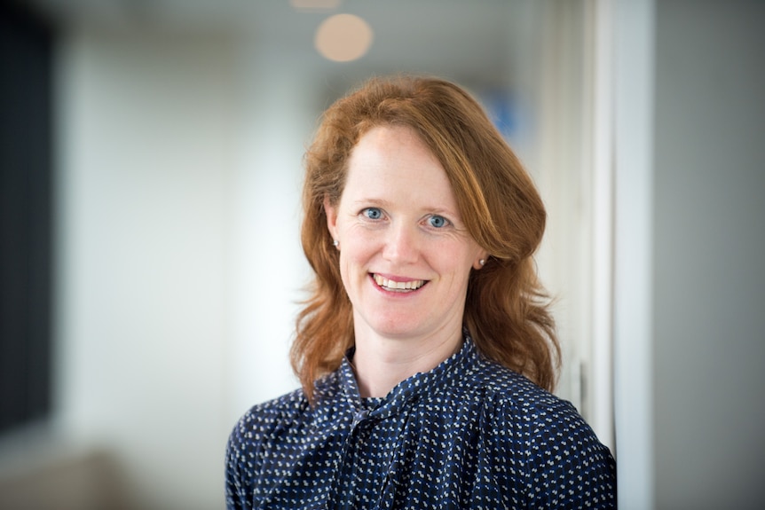 A woman with her hair and a dark blue shirt looking ahead, smiling.