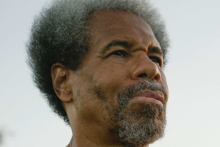 An African-American man with greying curly hair and beard looks to the right of the camera.