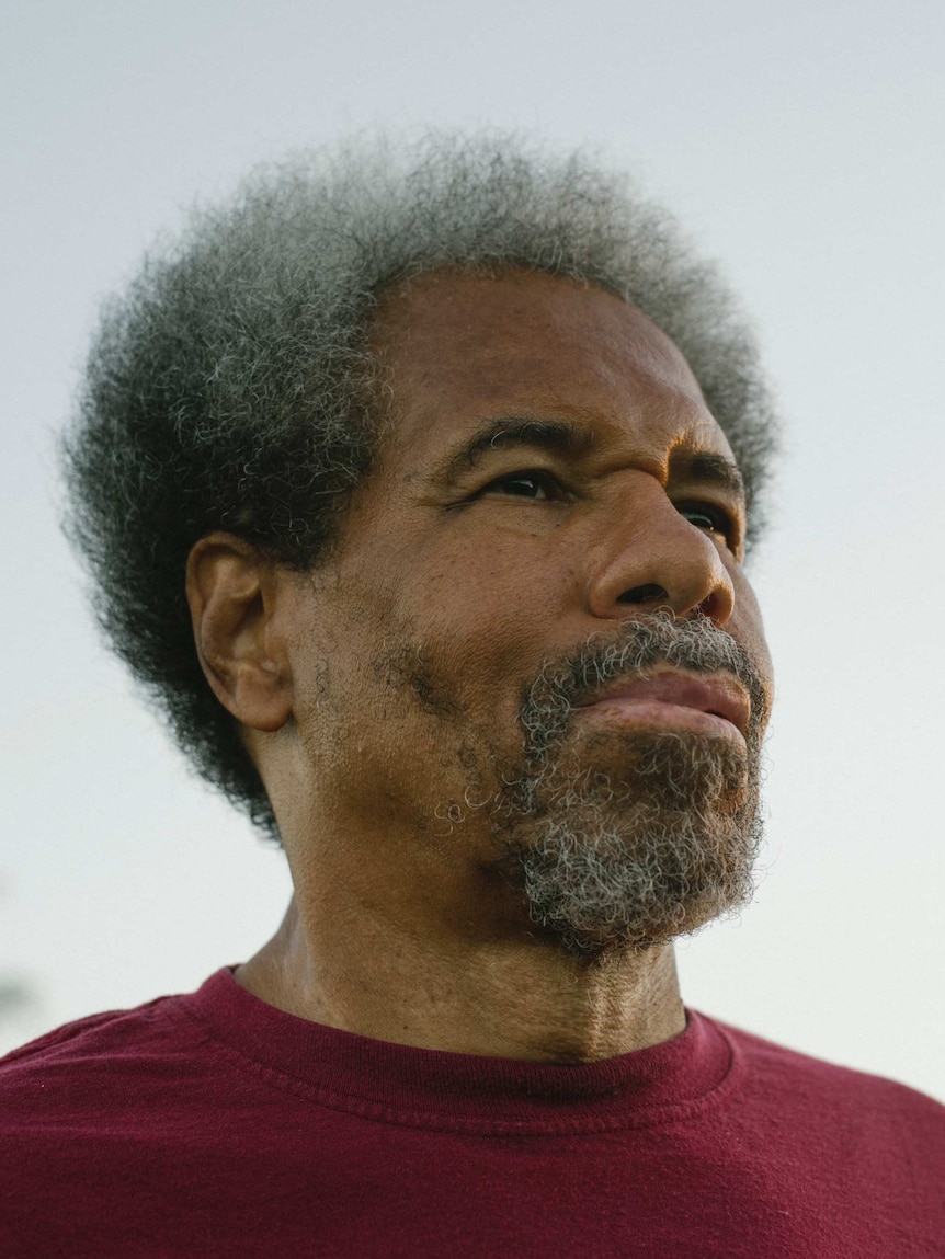 An African-American man with greying curly hair and beard looks to the right of the camera.
