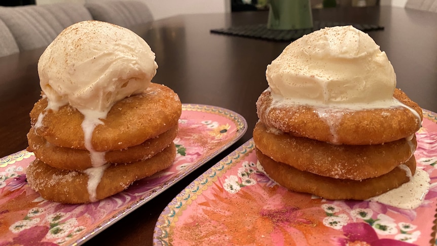 Two oblong-shaped plates, which each have a stack of three pineapple fritters and a scoop of ice cream on them.