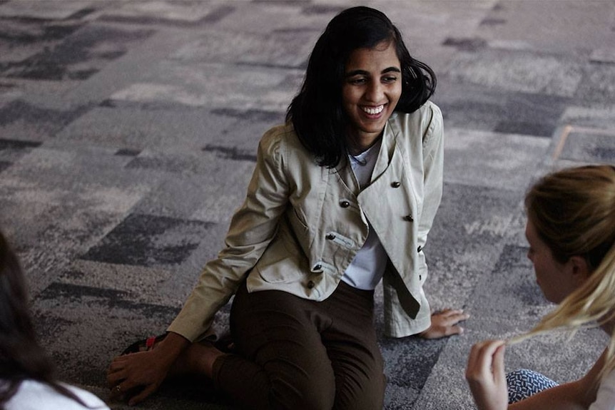 Image of a young woman —  Pritika Desai, founder of ShoutOut!, sitting on the ground chatting to people at an event.
