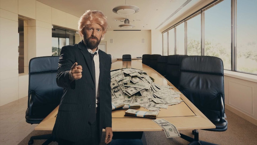 Christiaan Van Vuuren in a suit and wig with money on table behind him