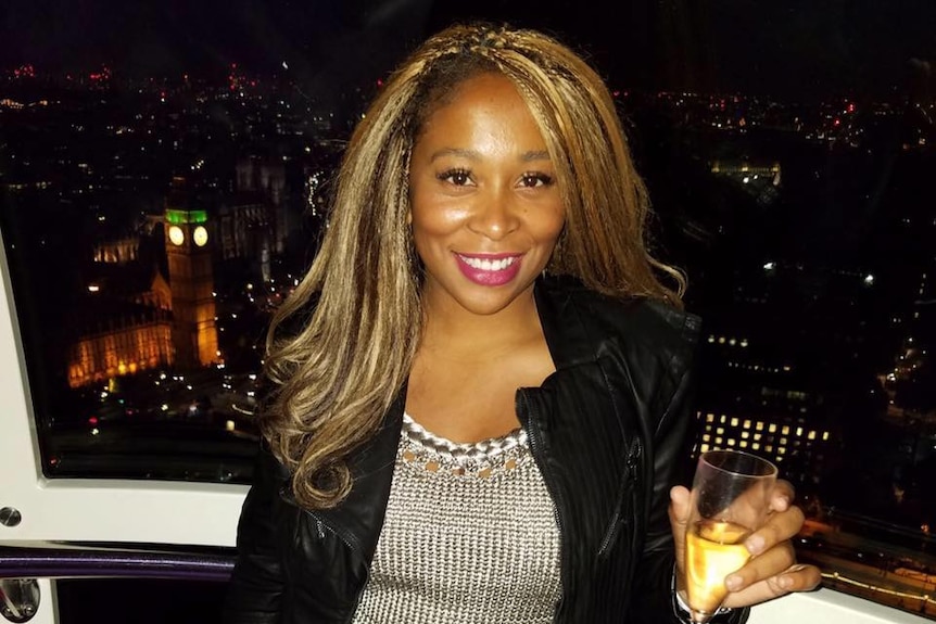 Adama Iwu stands on a balcony at night with a glass of champagne.