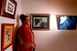 A woman looks sideways with a painting of a dog behind her.