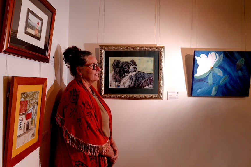 A woman looks sideways with a painting of a dog behind her.