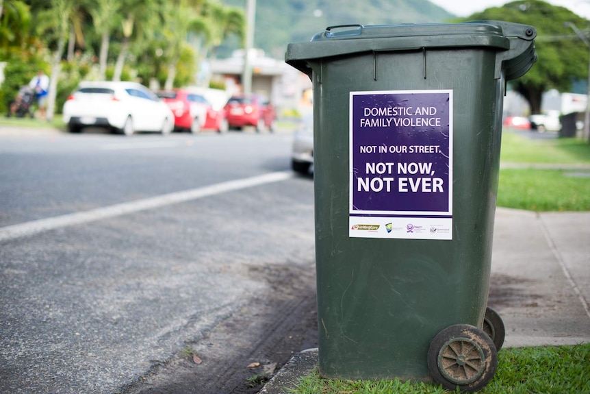 A wheelie bin with an anti-domestic violence sticker on its side awaits collection on the kerbside.