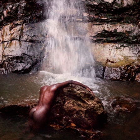 A naked Moses Sumney lies on a rock in a waterfall on the cover of Grae