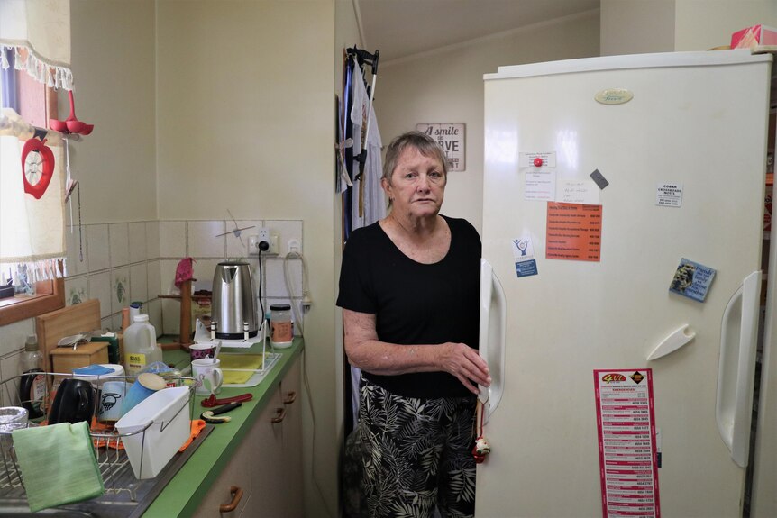 a woman stands in front of an open fridge in her small kitchen