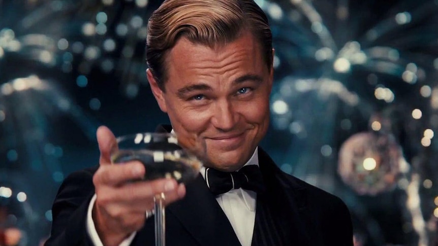 Leonardo DiCaprio looks offscreen and smirks while holding a drink up in character.