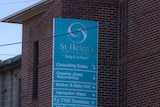 A blue hospital sign again st a red brick building and other old buildings.