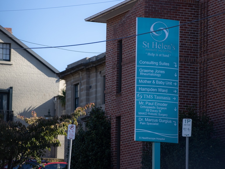 A blue hospital sign again st a red brick building and other old buildings.