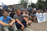 a group of men and woman, some with placards, sitting on road an chanting slogans