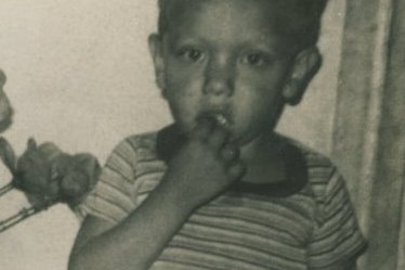 A young boy wears a striped shirt and holds his hand to his mouth.